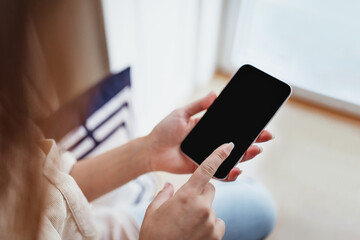 Millennial european woman typing on phone with empty screen, resting in minimalist living room interior