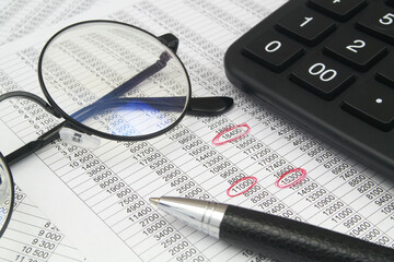 Accountancy and finding errors concept. Calculator, pen and eyeglasses on financial papers.