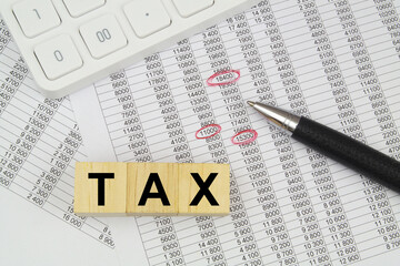 Letters tax on cubes, white calculator and black pen on financial reports.