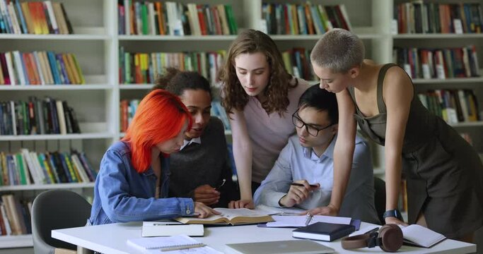 Group of diverse teens students gathered in library, studying together, learning topic read chapter in textbook looking interested and motivated to prepare for exams, engaged in teamwork in classroom