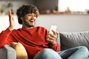 Good News. Happy Young Indian Man Looking At Smartphone Screen At Home