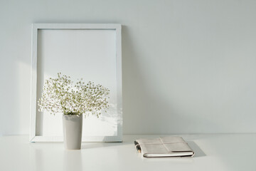 Empty picture frame, vase with flowers and planner on table