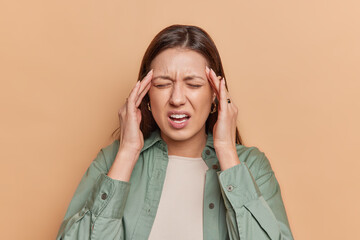 Exasperate brunette young woman suffers from terrible migraine or strong headache being overworked...