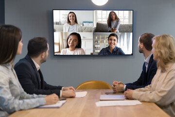 Office video conference meeting of diverse business team. Company coworkers sitting at negotiation table, talking to young multiethnic female customers, professionals, freelancers