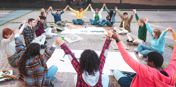 A group of multicultural peacefully activists are sitting with posters outside while holding hand by hand demonstrate against climate change - Global warming, pollution and climate change concept