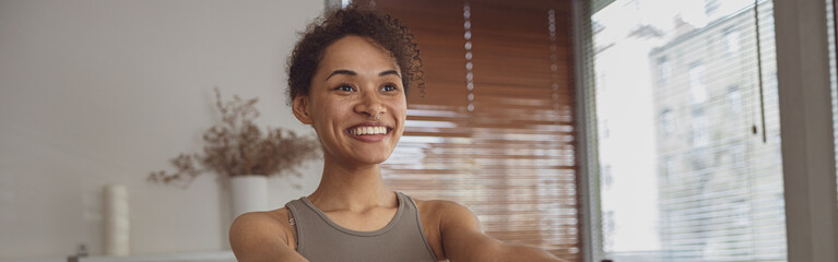 Slim woman doing exercises for hands with elastic band by online tutorials on laptop in living room