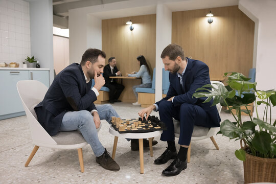 Two business professional men playing chess in office cafe, sitting at board, moving pieces, enjoying break, smart game, hobby, leisure time, entertainment, training intelligence, strategic skills