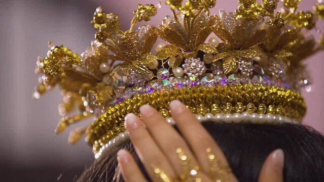 Hands of an Asian woman holding a golden crown or jada that adorns her head on her wedding day.