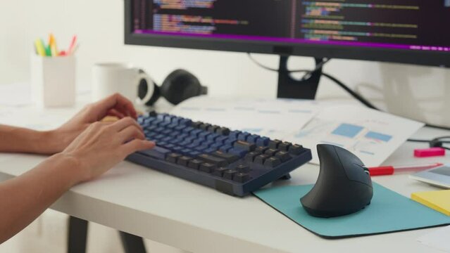 Close-up young Asia girl IT development programmer typing on keyboard coding programming fixing database code on computer monitor and laptop screen on table in workroom at house office.