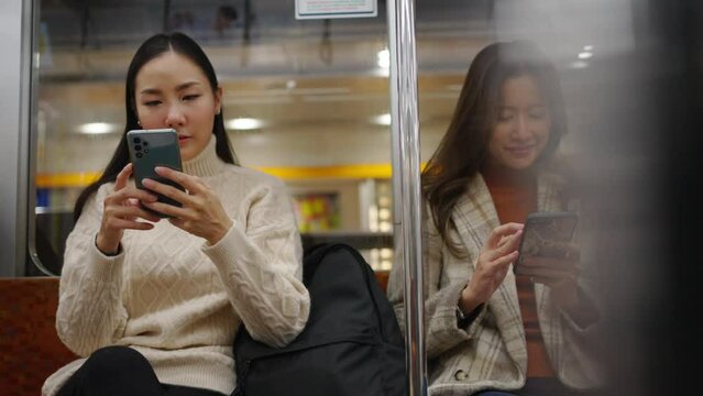 4K Asian woman using mobile phone text online message or searching data during travel on subway underground train. Young women enjoy urban lifestyle and commuting in city by railroad transportation.