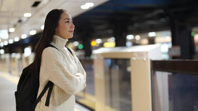 Portrait of Asian woman tourist waiting for the train at railway station at night. Attractive girl traveler enjoy urban lifestyle travel in the city by railroad transportation on holiday vacation.