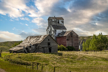 Rustic buildings and grain elevator stand in what used to be the town of Sharples Alberta Canada