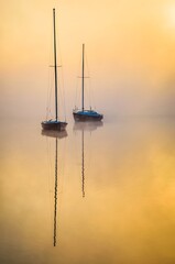 Minimalist morning landscape over a misty lake. Boats reflecting in the water at Lake Paprocany in Tychy, Poland. - 595564602