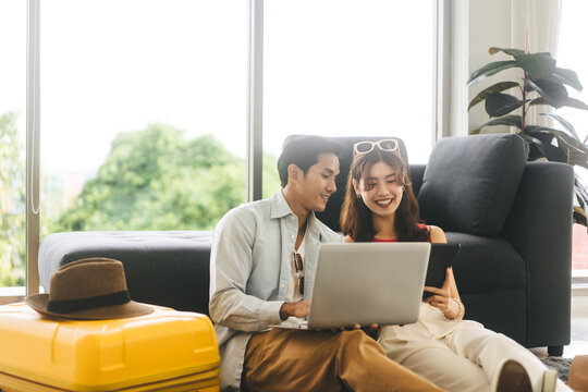 Young adult southeast asian couple using laptop for getting ready for holidays travel trip in living room at home