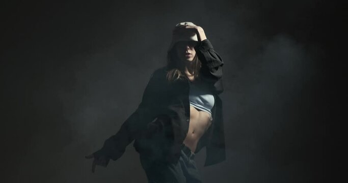 Stylish young woman dancing hip hop freestyle on smoky studio background