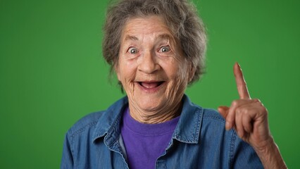 Extreme closeup of funny thinking thoughtful elderly old toothless woman with great idea points with finger on green screen background.