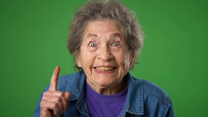 Closeup portrait of thinking, smart puzzled pensive elderly senior old woman with wrinkled skin and grey hair looks around thinks has great idea raised finger isolated green screen background