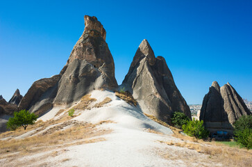 Fairy Chimneys rock formation in Cappadocia, Dark cone-shaped rocks stick out of the white ground with sparse vegetation and blue sky, Nature of Turkey Central Anatolia