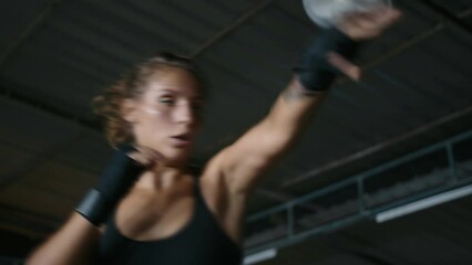 Woman boxer working out in gym ring. Portrait of female fighter wearing black sportswear and bandages practicing kicks and punches - Powered by Adobe