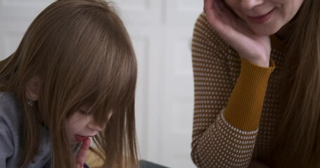 Slow motion shot of happy caucasian young mother helping cute daughters in writing homework on table at home