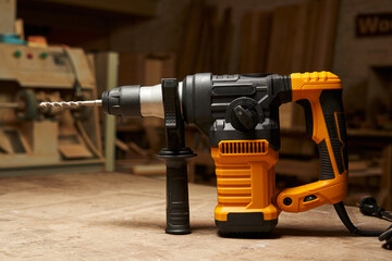 side view of a modern electric rotary hammer with vertical motor, mounted drill and additional handle. against the backdrop of a woodworking workshop
