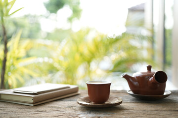 Earthenware teapot and tea cup and notebooks on wooden table