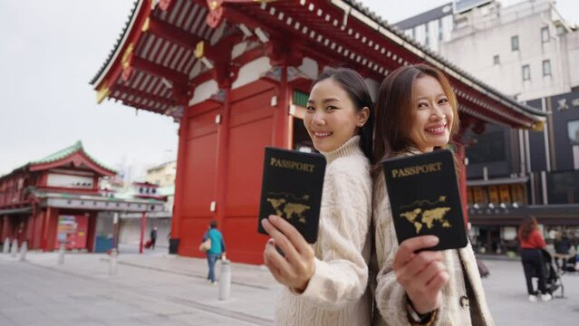 4K Two Happy Asian woman friends showing passport in front of Sensoji Temple in Asakusa Tokyo, Japan. People enjoy and fun travel Japan on holiday vacation. Global transportation airline concept.