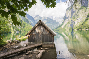 Old wooden boathouse with boardwalk on a pristine alpine lake surrounded by mountains, Obersee, Germany