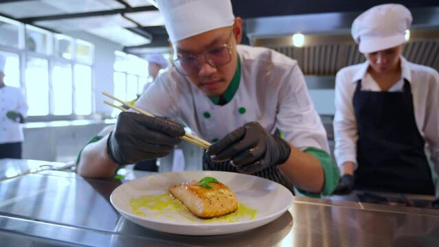 Closeup hands of chef man cooking salmon steak and decoration on plate with professional in kitchen at restaurant, food and garnish for serving, food japan, culinary and recipe with delicious.