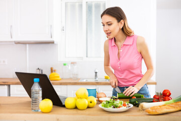 Young woman cooking vegetables for dinner and browsing sns on laptop