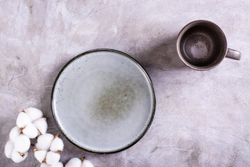 Mockup of empty ceramic plate, cup and cotton branch on gray background top view