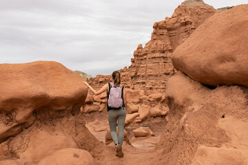 Woman hiking next to unique eroded Hoodoo Rock Formations at Goblin Valley State Park in Utah, USA, America. Sandstone rocks called goblins which are mushroom-shaped rock pinnacles. Canyon hike trail
