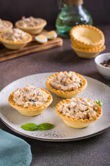Obraz na płótnie Canvas Appetizing tartlets with egg, canned tuna and onion salad on a plate on the table vertical view