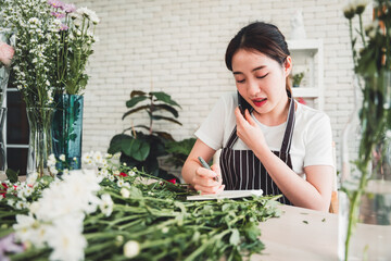 Obraz premium Young florist taking phone orders with smiling face in flower shop full of flowers and supplies.