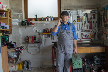 Image of a handyman in his workshop talking on the phone and holding a toolbox. Answering a call for work.
