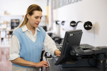 Woman working in publishing facility, using printer, pushing buttons on display.