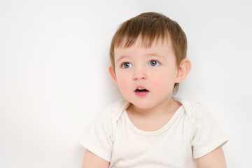 Naklejka premium Surprised baby looks up with open mouth, studio white background. Amazed child with an emotion of surprise on his face. Kid about two years old (one year nine months)