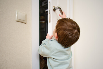 Little baby opens the door. Child pulls the door handle with the lock closed. Kid aged two years - obrazy, fototapety, plakaty
