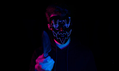 Young man in purge mask points finger while holding knife on black background.