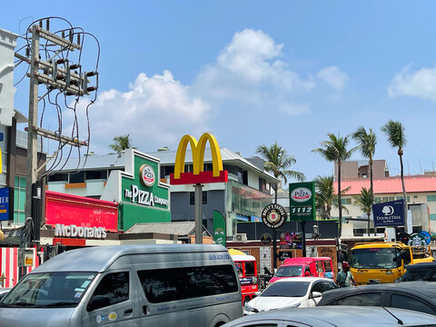 Patong Beach, sea street, first line. Phuket island, Thailand. Many cars on the road. Bright signs and logos of famous companies: Starbucks, McDonald's, Pizza, etc. Tropical tourist town. Day time. 