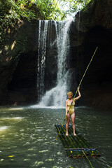 A young, sexy girl in a yellow swimsuit floats on a bamboo raft along the river, against the...