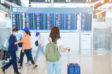 Young woman with bag and luggage looking to flight time information board in international airport, before check in. Travel, Vacation, trip and Transport concept