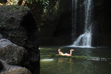 A young sexy girl in a yellow swimsuit bathes in a river with a waterfall in Bali.