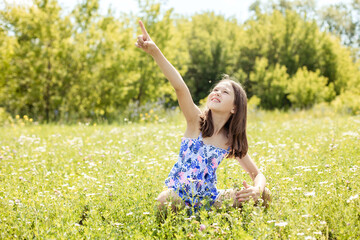 Teenage girl sitting on the grass in the park points her hand up to the sky