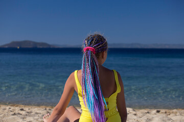 teenage girl with colored hair extension braids on sunny tropical blue beach