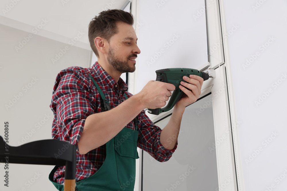 Sticker Worker in uniform installing roller window blind indoors