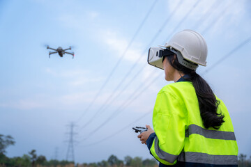 A female electrical engineer wearing vr goggles inspects site using drone survey aerial view of high voltage pylons at power station to plan electric power generation at high voltage pylons.