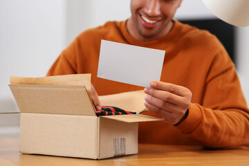 Young man holding greeting card near parcel with Christmas gift, closeup