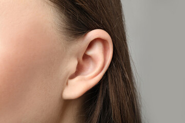 Woman touching her ear on light grey background, closeup