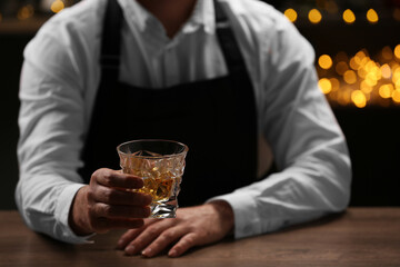 Bartender with glass of whiskey at bar counter indoors, closeup